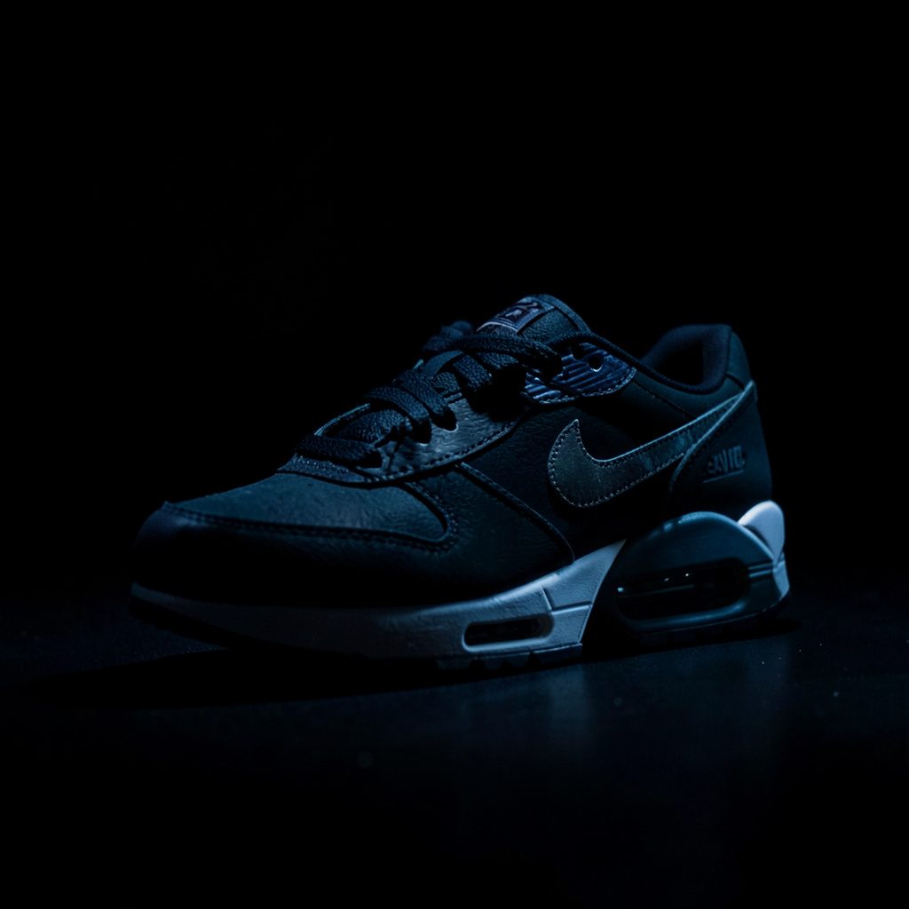 Donkere, sfeervolle close-up van een Nike Air Max sneaker met zichtbare luchtzool, in diepe zwarte en bruine tinten met subtiel licht