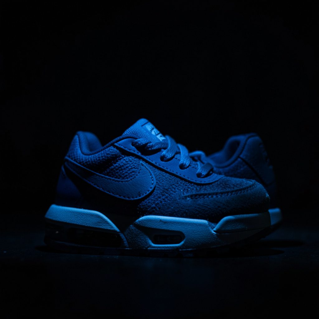 Nike sneakers voor kinderen in lichte tinten, gefotografeerd van dichtbij op een donkere achtergrond met zachte schaduw
