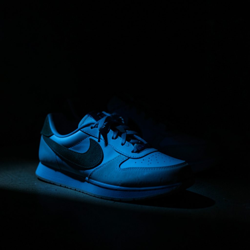 Verschillende Nike dames sneakers in wit, zwart en pastelroze gegroepeerd, met dramatische low-key belichting en diepe schaduwen.
