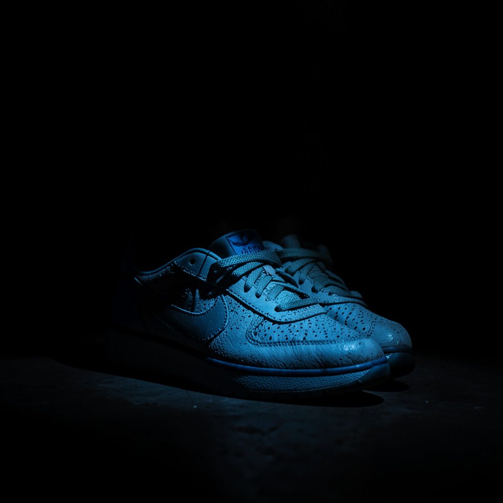Close-up van elegante Nike dames sneakers in wit en zachtroze, met diepe schaduwen die de textuur van het bovenwerk accentueren.